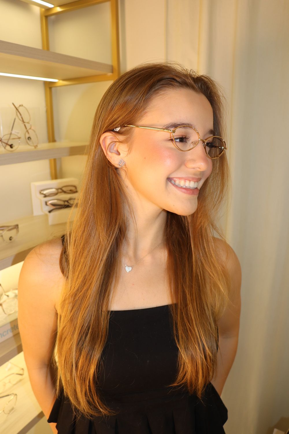 Cliente sorrindo com armação dourada dentro da loja Excellence Óticas